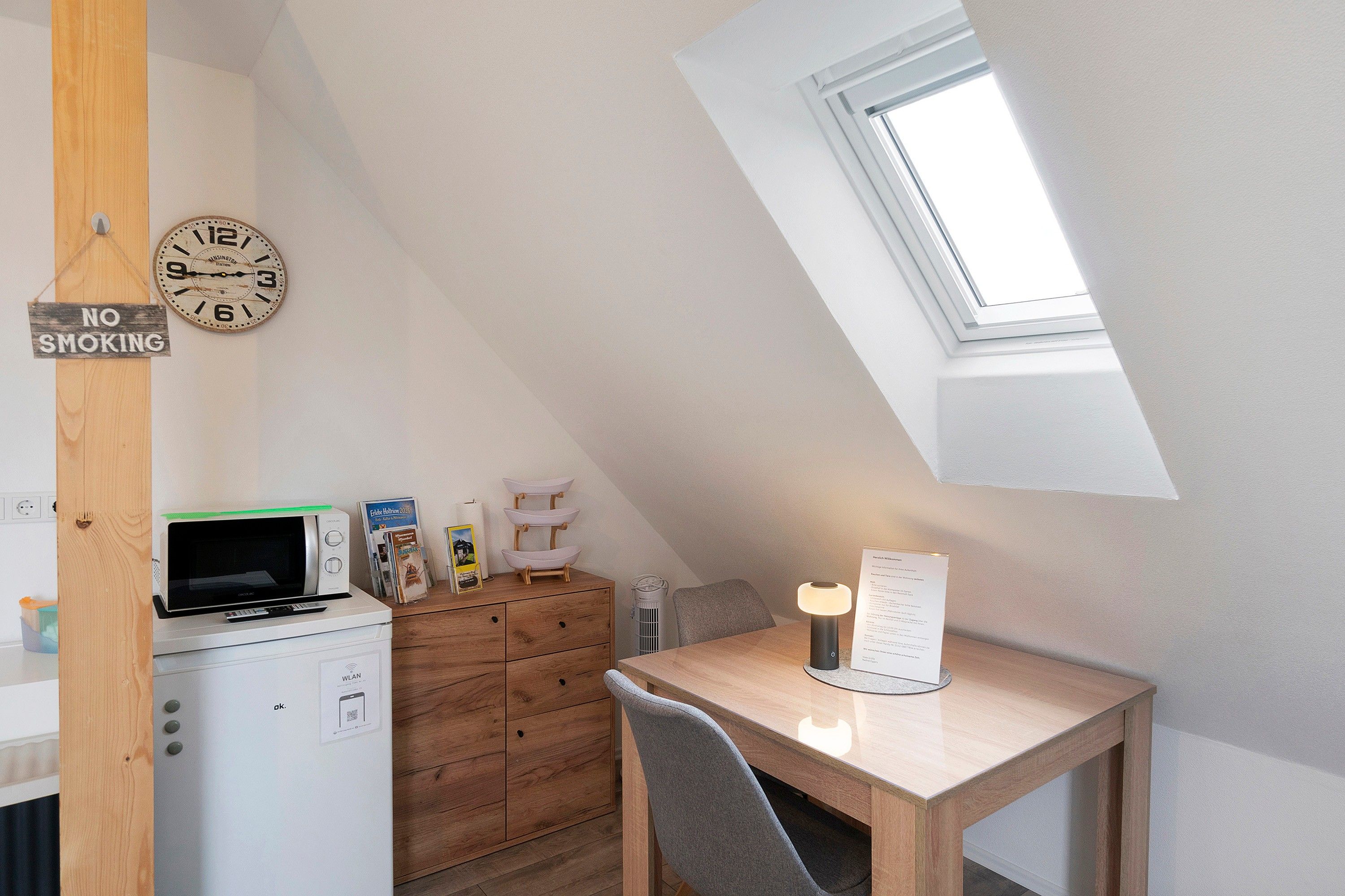 A small, modern kitchen with a microwave, a wooden cabinet, and a 'NO SMOKING' sign.