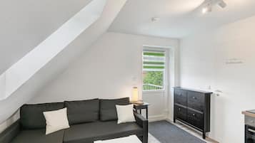 Un salon moderne avec un canapé foncé, une petite table d’appoint, un téléviseur à écran plat et une porte donnant sur un balcon.