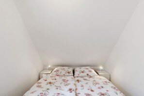 Una habitación pequeña y ordenada con una cama, mesitas de noche y una lámpara.