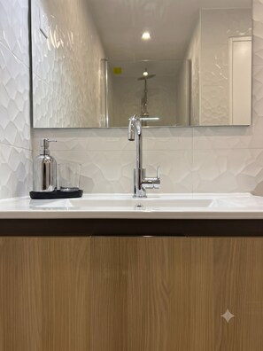 A bathroom with a white sink, a mirror, and a shower. - Celine 10 (Paris)