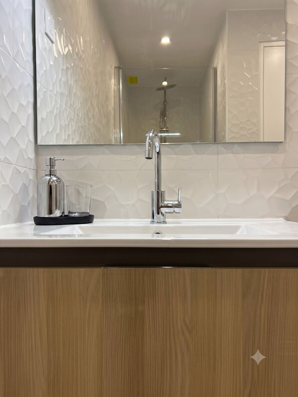 Un bagno con un lavandino bianco, uno specchio e una doccia.