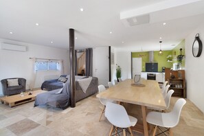 A modern living space with a sofa, a dining table with chairs, a kitchen area, and a staircase. - Holiday Home 'Maison De Vacances L Etable' with Private Pool, Wi-Fi and Air Conditioning (Coly-Saint-Amand)