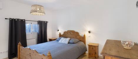 Ein Schlafzimmer mit einem hölzernen Bett, einem Nachttisch, einer Kommode und einer Pendelleuchte.