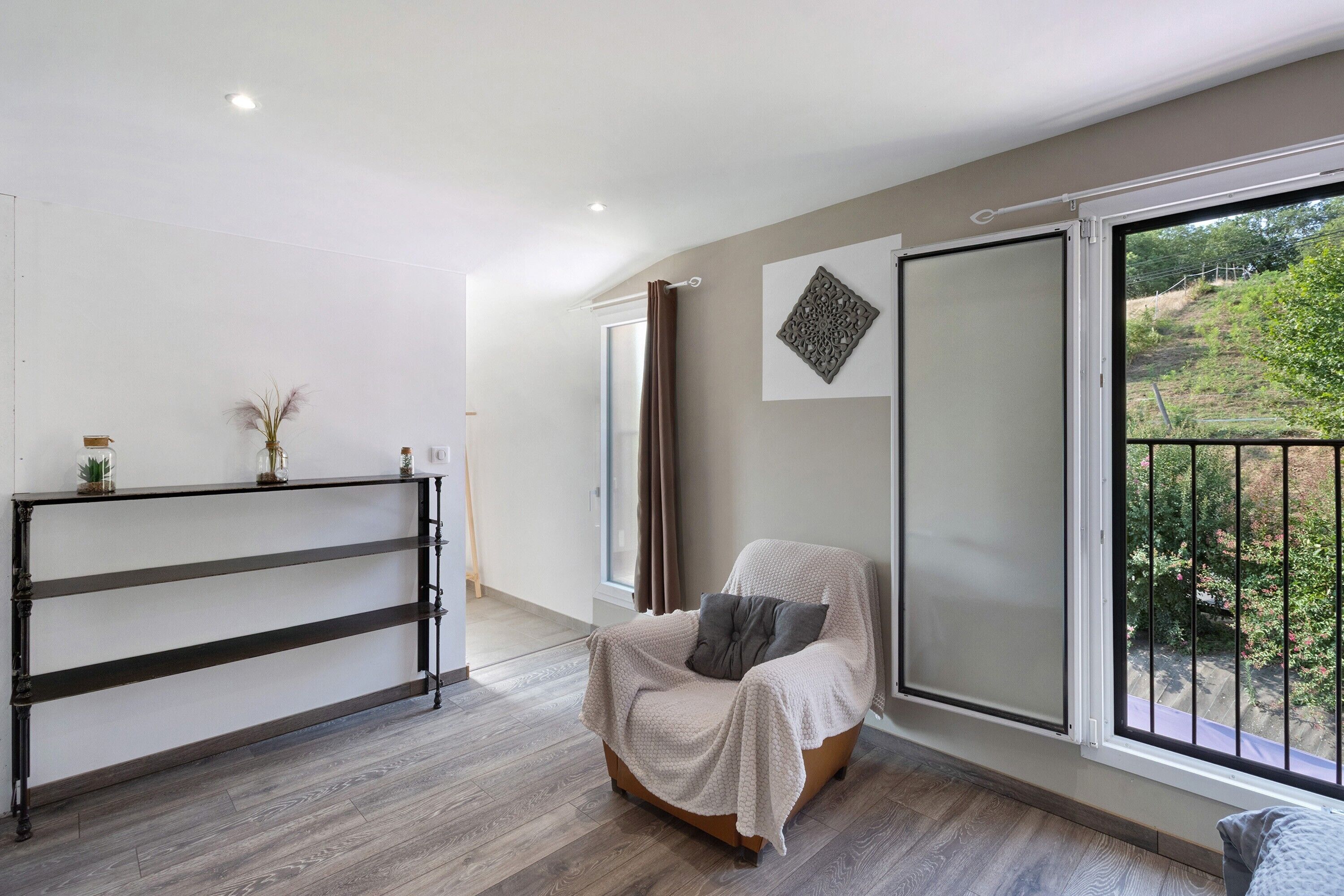 A modern living room with a large window, a sofa, a wooden floor, and a decorative wall piece.