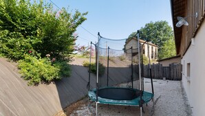 Un jardin avec un trampoline, une clôture en bois et un bâtiment en arrière-plan.