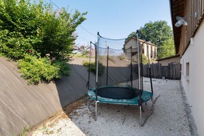 Ein Garten mit Trampolin, Holzzaun und einem Gebäude im Hintergrund.