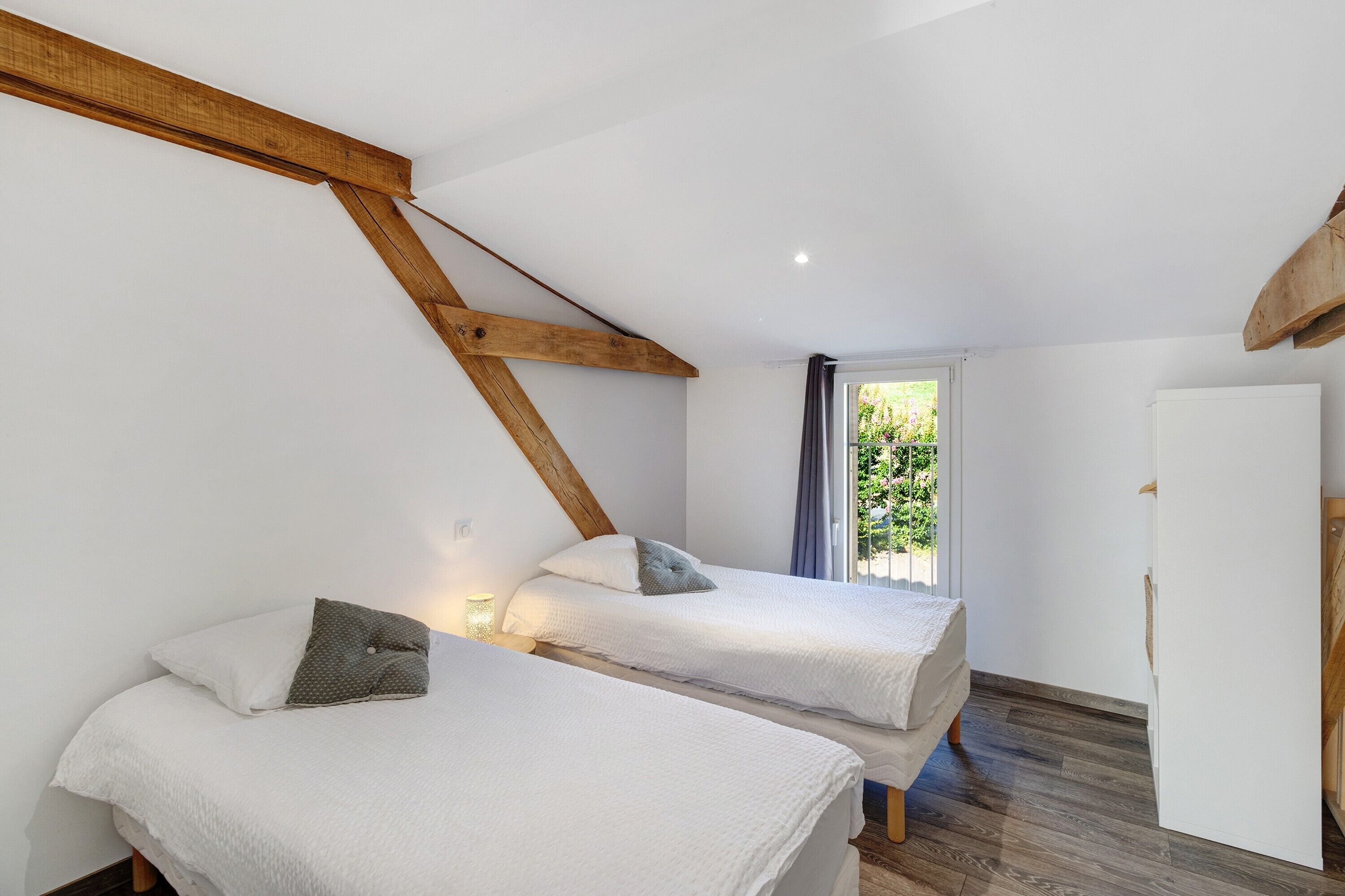 Ein Schlafzimmer mit zwei Betten, Holzbalken, einem fenster mit Vorhängen und einer weißen Tür.