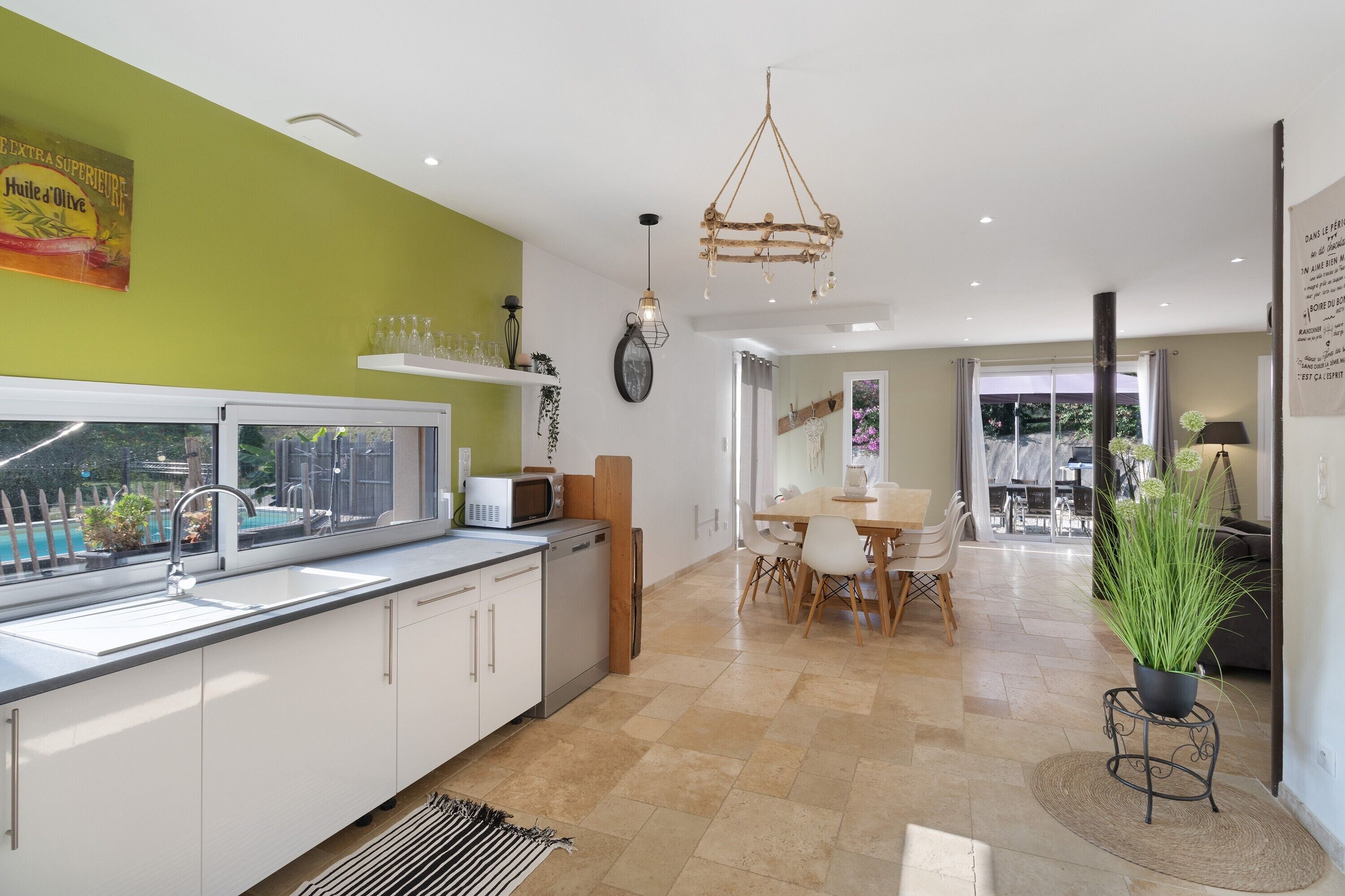A modern kitchen with a view of a pool, a dining area with a table and chairs, and a living space with a plant.