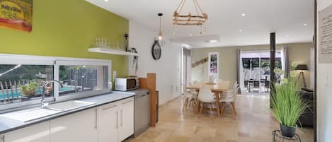 A modern kitchen with a view of a pool, a dining area with a table and chairs, and a living space with a plant.