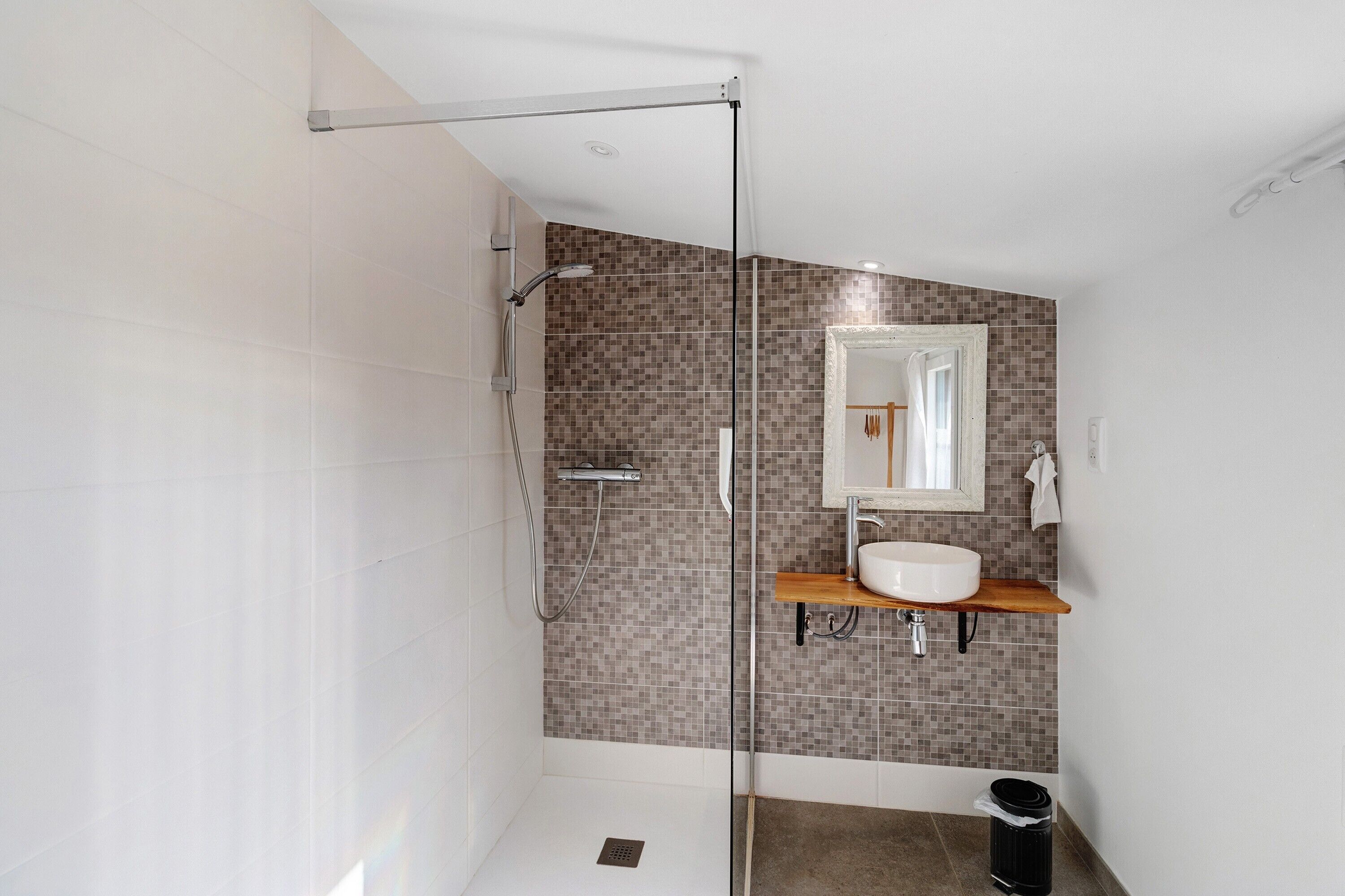 Une salle de bain moderne avec une douche à parois de verre, un lavabo blanc et un mur recouvert de carreaux.
