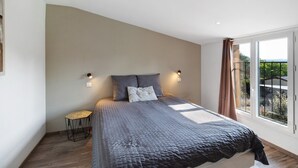 Une chambre avec un grand lit, deux lampes fixées au mur, une petite table de chevet et une vue par la fenêtre.