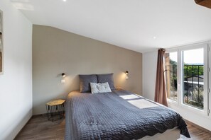 Ein Schlafzimmer mit einem großen Bett, zwei Wandleuchten, einem kleinen Nachttisch und Blick durch ein Fenster.