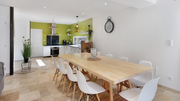 Une cuisine moderne avec des meubles blancs, un mur d’accent vert et un coin repas comprenant une table en bois et des chaises blanches.