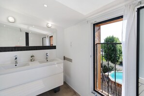 Ein Badezimmer mit einem Doppelwaschbecken, einem Spiegel und einem Fenster mit Blick auf einen Swimmingpool.