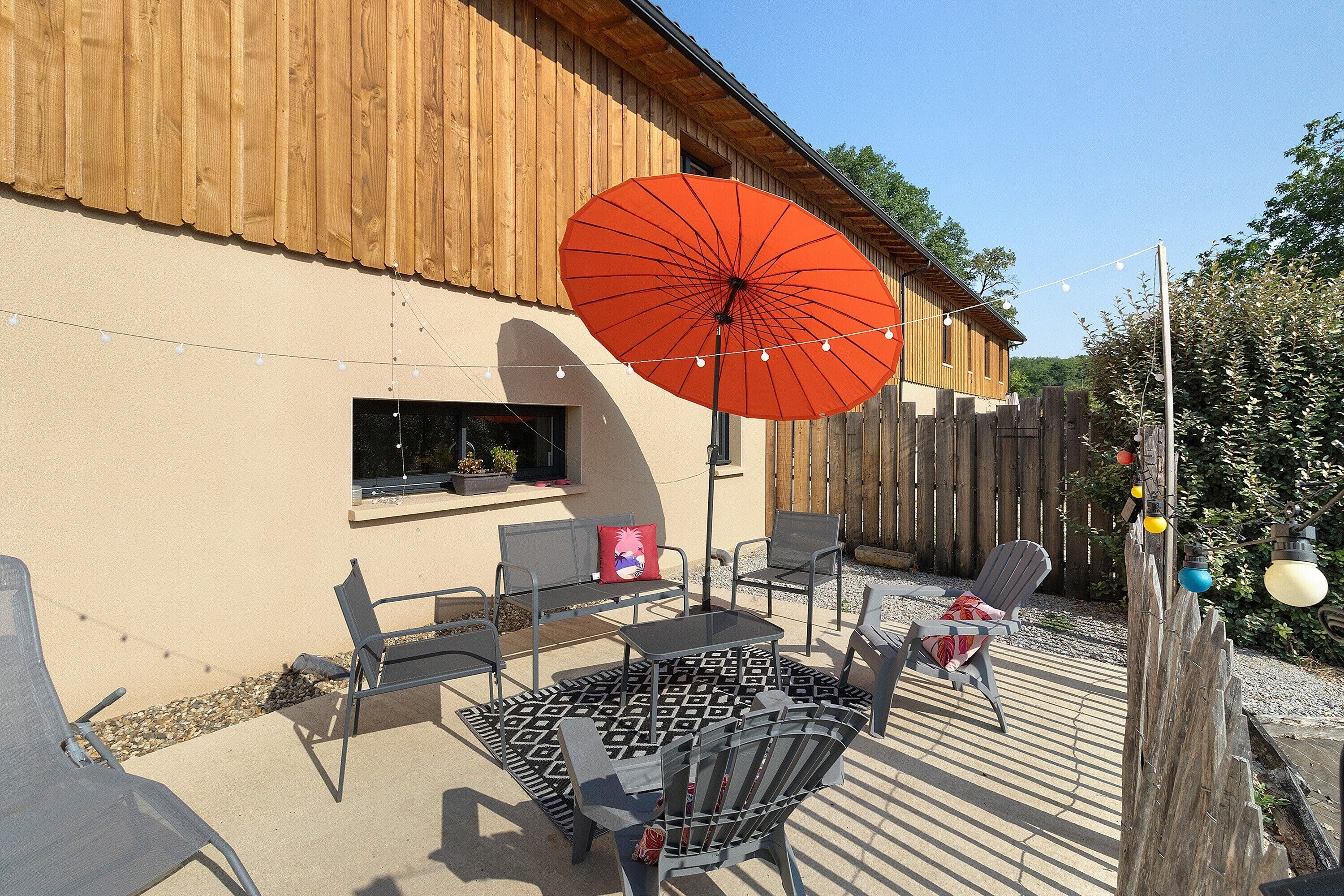 Une terrasse extérieure avec une table et des chaises, un parasol rouge et une clôture en bois.