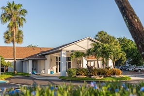 A hotel with a covered entrance, palm trees, and a parking lot. - Peaceful Stay | Pool+Garden Area, Views, BBQ (Kissimmee)