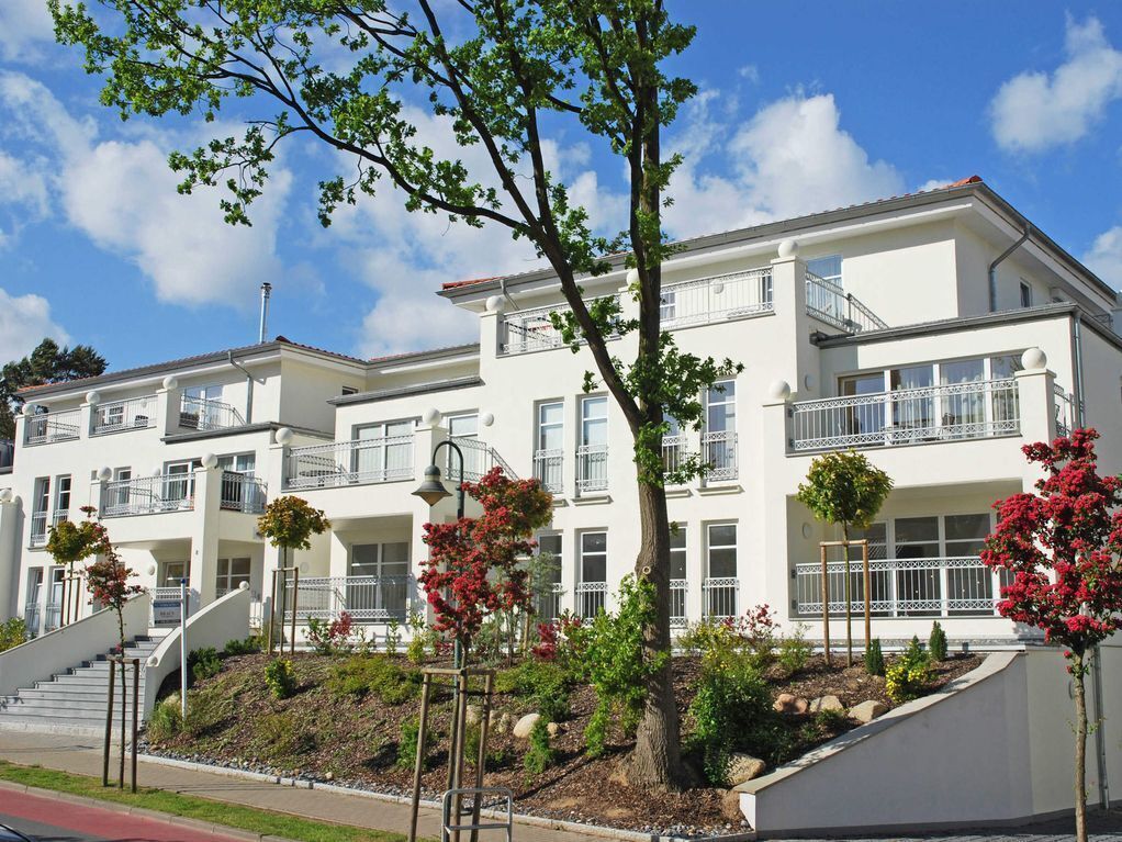 A multi-story residential building with balconies, a landscaped garden, and a clear sky.