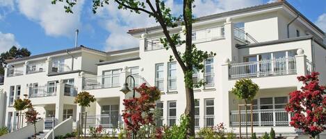 A multi-story residential building with balconies, a landscaped garden, and a clear sky.