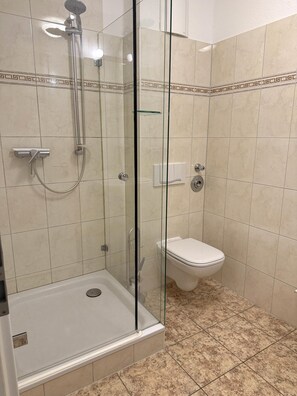 A shower area with a glass door, a handheld showerhead, and a wall-mounted faucet. - Dünenresidenz Königin Augusta 2 in Binz (Ostseebad Binz)