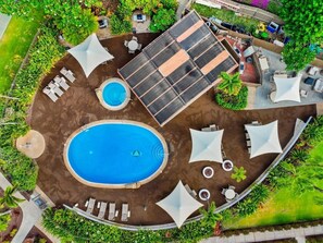 Vue aérienne d’un espace piscine comprenant une piscine circulaire, des chaises longues, des parasols et un ensemble de panneaux solaires.
