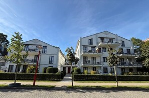 Un edifici d'apartaments modern amb múltiples balcons, una entrada pavimentada i respectables taronja.