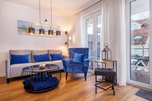 Ein modernes Wohnzimmer mit einer Couch, einem Sessel, einem Couchtisch und einem Beistelltisch mit einer Lampe.