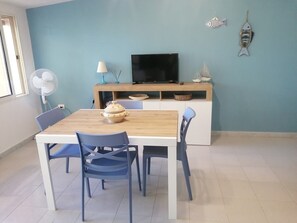Un comedor con una mesa de madera y sillas azules, un televisor sobre un mueble de madera y objetos decorativos en la pared.
