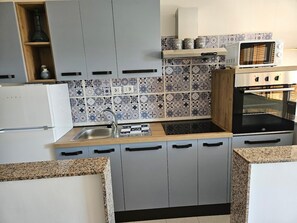 Una cocina con armarios grises, una encimera de madera, microondas, horno y salpicadero de azulejos.