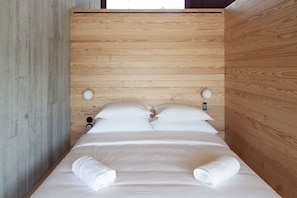 Uma cama com cabeceira de madeira, roupa de cama branca e duas toalhas brancas sobre a cama.