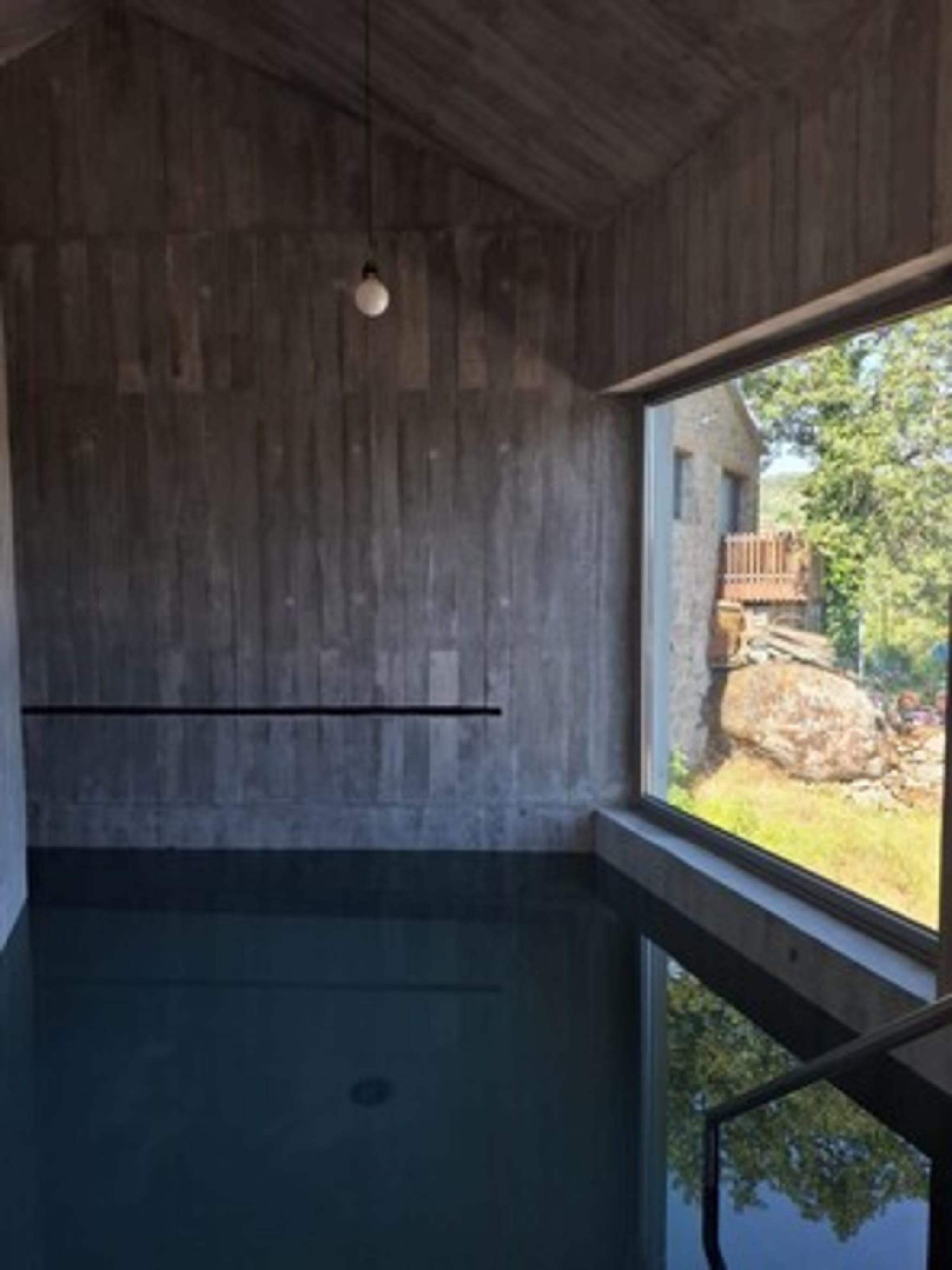 Una habitación con un ventanal grande, techo de madera y vistas a una construcción de piedra.