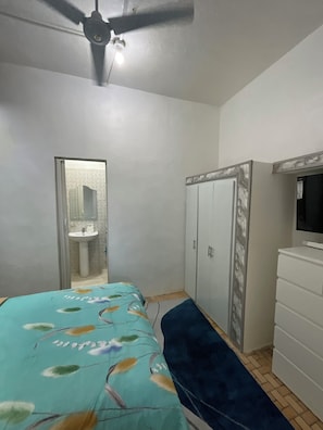 Ein Schlafzimmer mit Bett, Kleiderschrank, Fernseher und Deckenventilator.