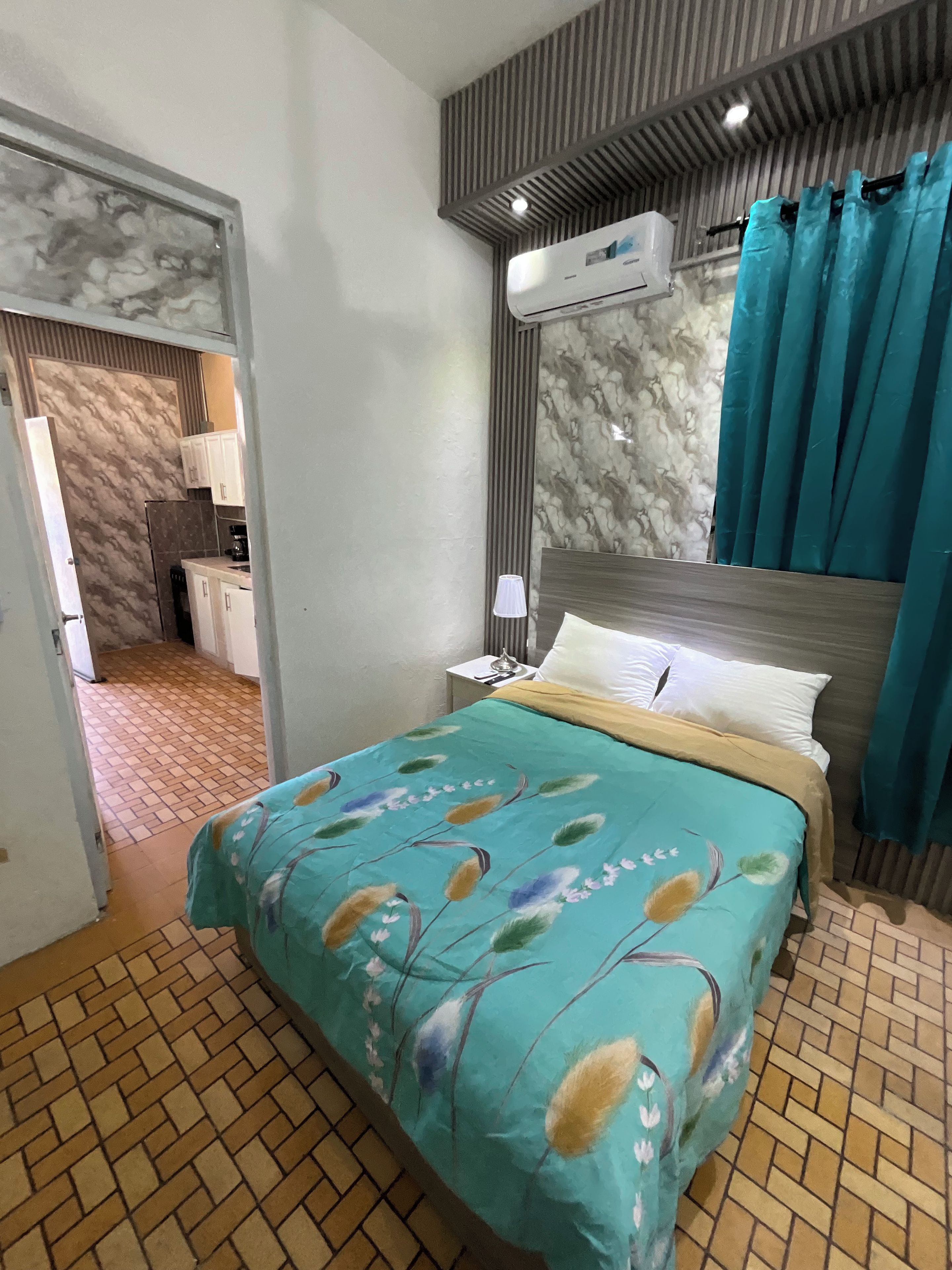 A hotel room with a bed, a nightstand, an air conditioning unit, and a bathroom visible through an open door.