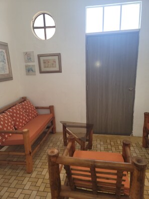 Ein Zimmer mit einer Holzbank, einem kleinen Tisch und einer Tür. An den Wänden hängen gerahmte Bilder.