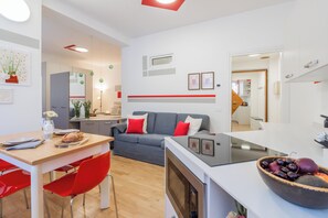 A modern living room with a dining area, a grey sofa with red cushions, a wooden dining table, and a kitchen area in the background. - Nineteen by Rent All Como (Como)