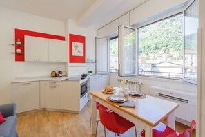 A modern kitchen with white cabinets, a wooden countertop, and red chairs. - Nineteen by Rent All Como (Como)