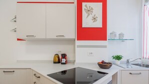A modern kitchen with a black induction cooktop, a kettle, a coffee maker, and a bowl of fruit on the counter. - Nineteen by Rent All Como (Como)