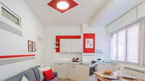 A compact living space with a kitchenette, a dining area, and a seating area with a sofa and red cushions. - Nineteen by Rent All Como (Como)