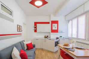 Ein kompakter Wohnbereich mit Küchenzeile, Essbereich und Sitzgelegenheit mit Sofa und roten Kissen.