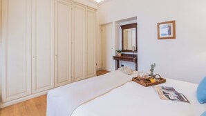 A bedroom with a large wardrobe, a bed with a white duvet, a bedside table with a mirror, a framed picture, and a small plant. - Churchkey by Rent All Como (Como)