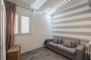 A room with a grey sofa, a window with curtains, a ceiling with skylights, and a striped wall. - Churchkey by Rent All Como (Como)