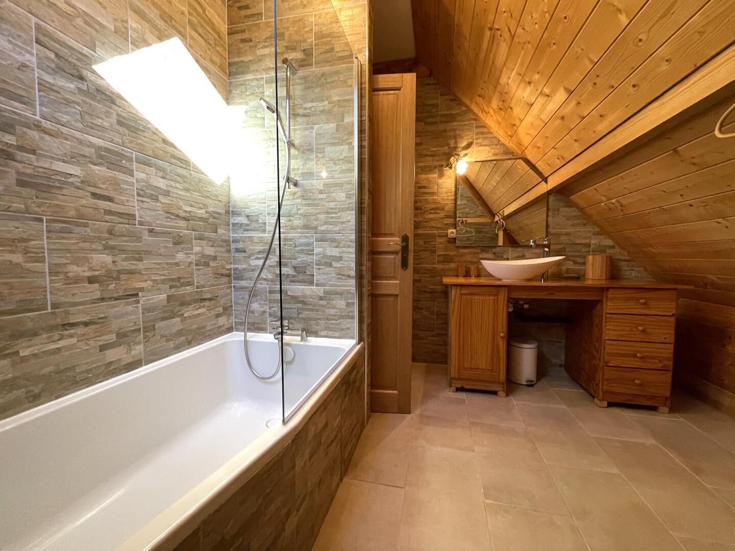 A modern bathroom with a stone wall, a bathtub, a wooden vanity, and a shower.