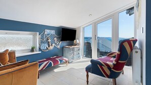 Een moderne woonkamer met een groot raam, een televisie en een fauteuil met een Union Jack dessin.