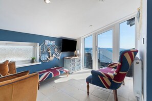 Ein modernes Wohnzimmer mit einem großen Fenster, einem Fernseher und einem Sessel mit Union Jack Design.