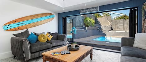 A modern living room with a pool, grey sofas, a wooden coffee table, and a ceiling with skylights.