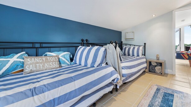 Een slaapkamer met een blauwe wand, twee bedden met gestreept beddengoed, een hoofdbord en een nachtkastje met een lamp.
