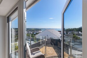 Un balcon donnant sur un quartier résidentiel, un immeuble avec un toit en pente et un ciel dégagé.