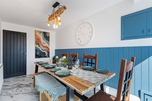 Un coin repas avec une table en bois dressée pour quatre personnes, une grande horloge murale et un mur d’accent bleu.