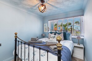 A bedroom with a bed, a window with blinds, a bedside lamp, and a ceiling fan. - Vitamin Sea - Swimming Pool, Hot Tub, Sea Views (Saundersfoot)