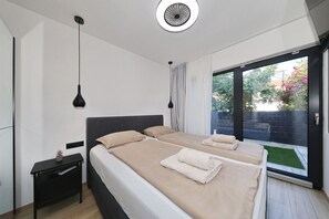A modern bedroom with two beds, a desk, and a large sliding glass door to a garden. - Beachfront Almare Retreat (Sukošan)