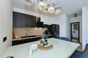 A modern kitchen with dark cabinets, a central island, and a dining area with a blue sofa. - Beachfront Almare Retreat (Sukošan)